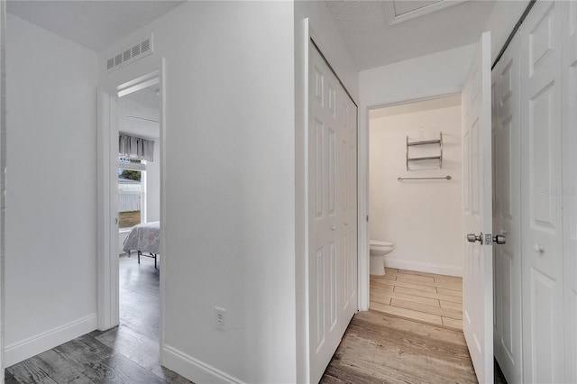 hall featuring visible vents, baseboards, a textured ceiling, and wood finished floors