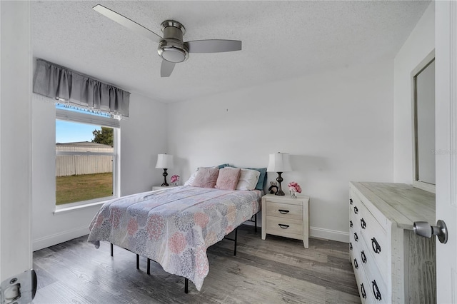 bedroom with a ceiling fan, wood finished floors, baseboards, and a textured ceiling