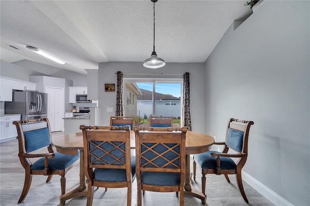 dining space featuring a textured ceiling, light wood-type flooring, and baseboards