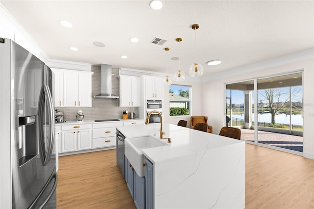 kitchen featuring wall chimney range hood, white cabinetry, hanging light fixtures, stainless steel appliances, and a water view