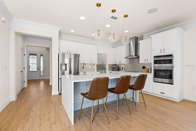 kitchen with white cabinets, stainless steel appliances, hanging light fixtures, and wall chimney exhaust hood