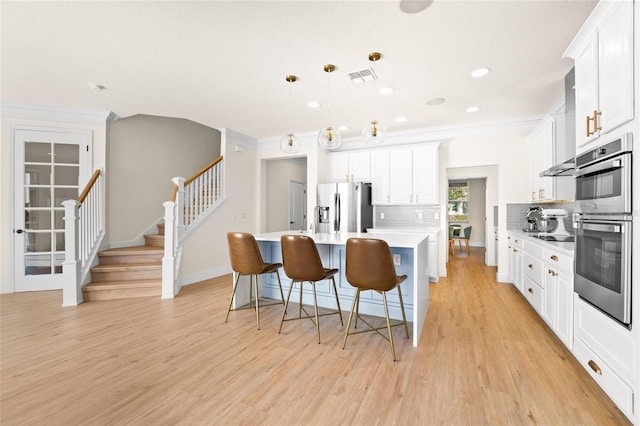 kitchen with a kitchen bar, white cabinetry, decorative light fixtures, an island with sink, and stainless steel appliances