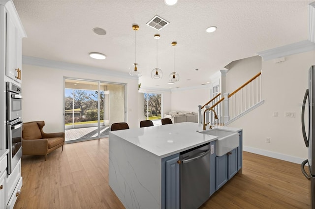 kitchen with decorative light fixtures, blue cabinets, white cabinets, a kitchen island with sink, and stainless steel appliances