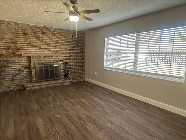 unfurnished living room featuring brick wall, a fireplace, ceiling fan, dark wood-type flooring, and a textured ceiling