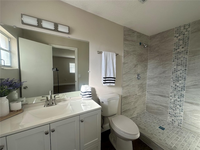 bathroom with vanity, a healthy amount of sunlight, a tile shower, and toilet