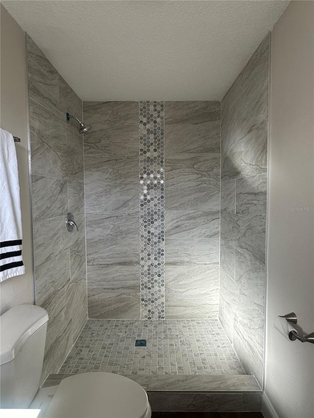 bathroom featuring tiled shower, toilet, and a textured ceiling