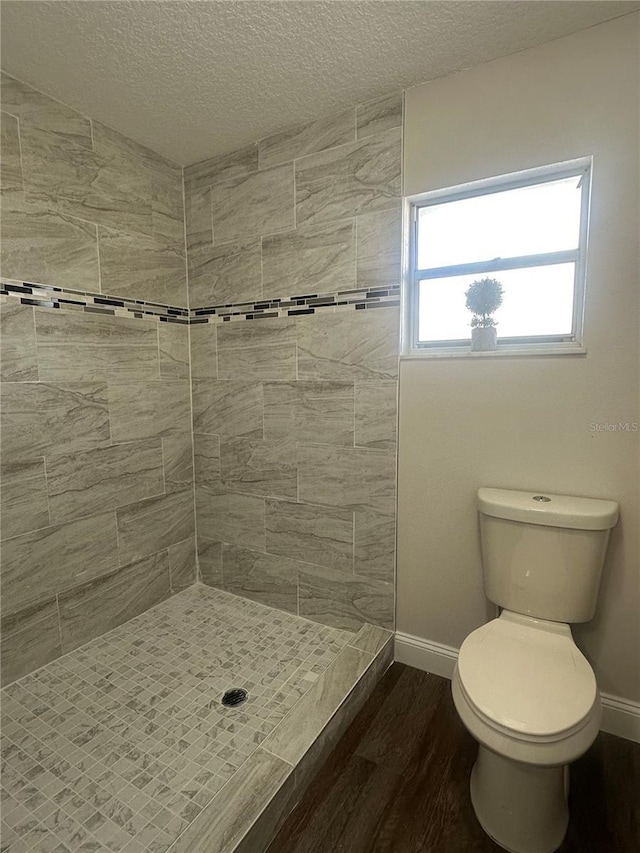 bathroom featuring a textured ceiling, wood-type flooring, toilet, and tiled shower