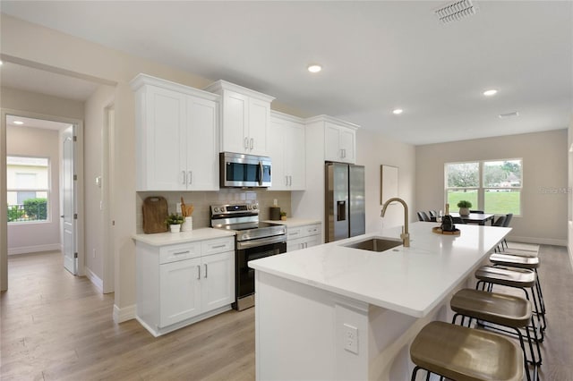 kitchen with white cabinetry, appliances with stainless steel finishes, sink, and a center island with sink