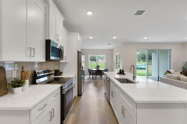 kitchen with light stone counters, stainless steel appliances, sink, and a center island with sink