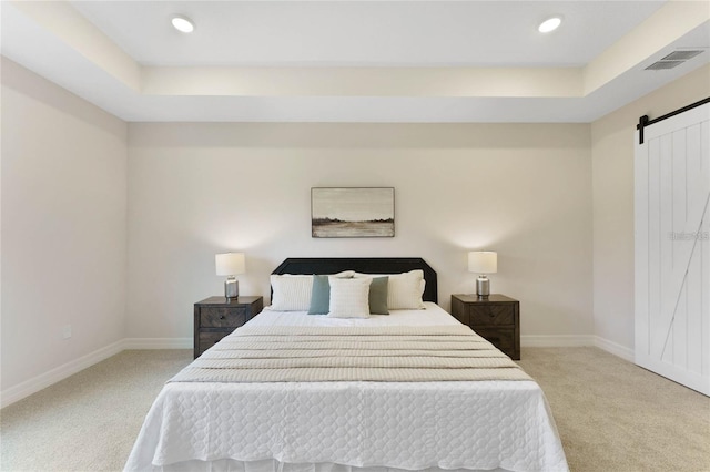 bedroom featuring a raised ceiling, a barn door, and light carpet