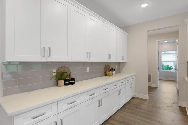 kitchen with white cabinetry, backsplash, wood-type flooring, and light stone countertops