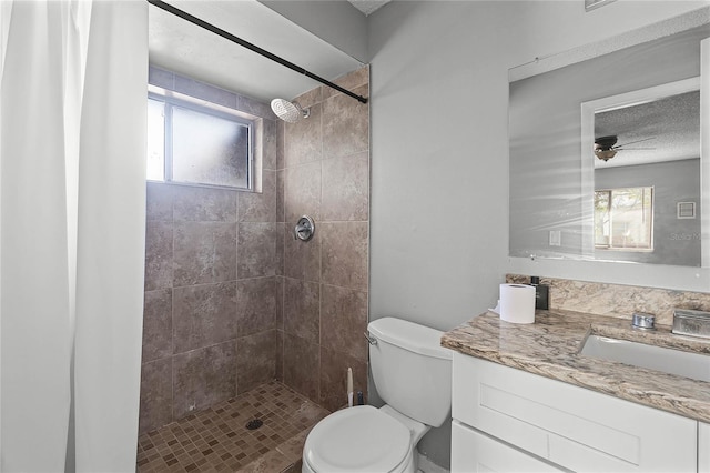 bathroom featuring a tile shower, vanity, toilet, and ceiling fan