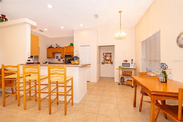 kitchen with light tile patterned flooring, a breakfast bar area, stainless steel oven, a notable chandelier, and kitchen peninsula