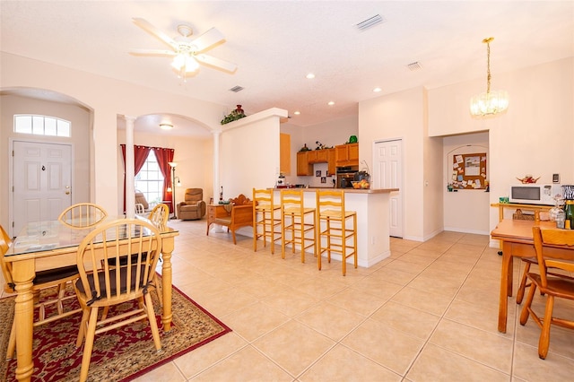 dining area featuring light tile patterned flooring, decorative columns, ceiling fan with notable chandelier, visible vents, and arched walkways