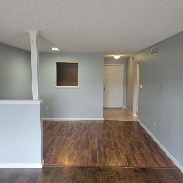 unfurnished room with hardwood / wood-style flooring, decorative columns, and a textured ceiling