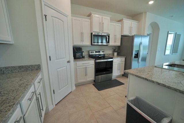 kitchen featuring sink, white cabinetry, light stone counters, light tile patterned floors, and appliances with stainless steel finishes