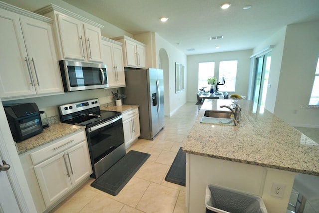 kitchen with sink, white cabinetry, stainless steel appliances, light stone counters, and a center island with sink