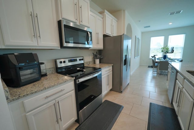 kitchen with white cabinetry, light stone counters, stainless steel appliances, and light tile patterned flooring