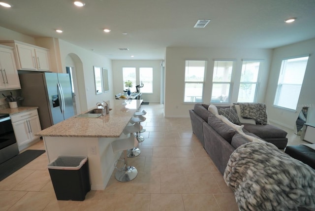 kitchen with sink, white cabinets, a kitchen bar, a kitchen island with sink, and light stone counters