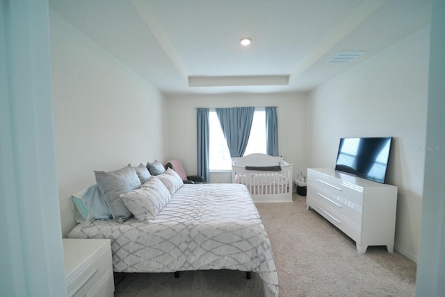 bedroom featuring light colored carpet and a raised ceiling