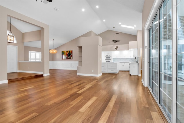 unfurnished living room with high vaulted ceiling, sink, ceiling fan with notable chandelier, and light wood-type flooring