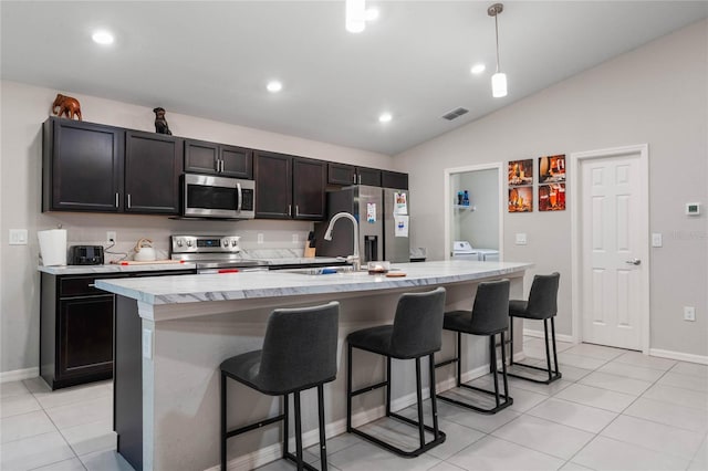 kitchen with vaulted ceiling, washer and dryer, a kitchen breakfast bar, a kitchen island with sink, and stainless steel appliances