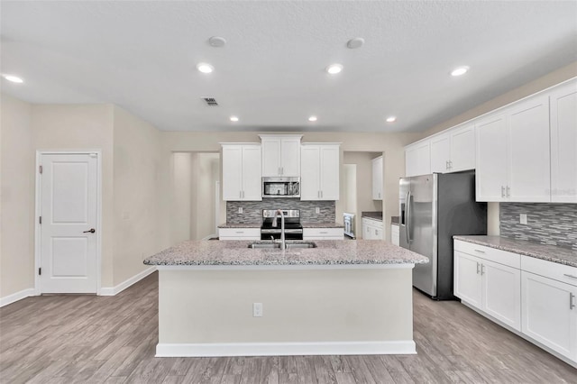 kitchen featuring appliances with stainless steel finishes, white cabinetry, an island with sink, sink, and light stone counters