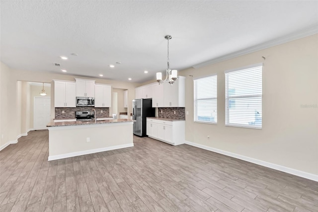 kitchen with decorative light fixtures, appliances with stainless steel finishes, an island with sink, decorative backsplash, and white cabinets