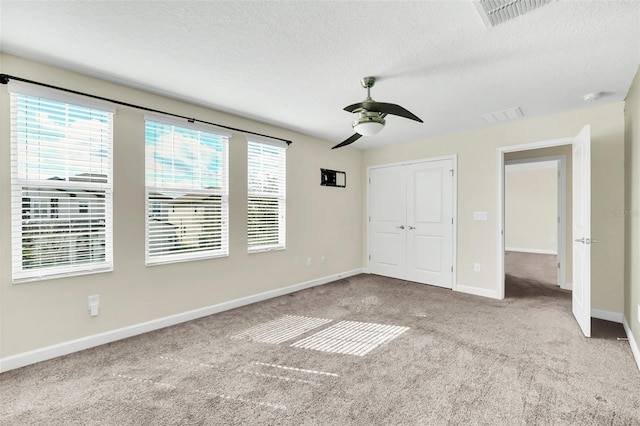 unfurnished bedroom with light carpet, ceiling fan, a closet, and a textured ceiling