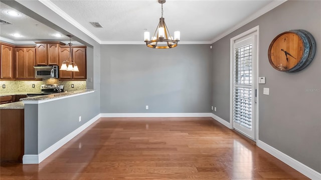 kitchen with dark wood-type flooring, light stone counters, hanging light fixtures, ornamental molding, and stainless steel appliances