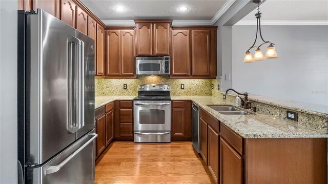 kitchen with decorative light fixtures, sink, kitchen peninsula, stainless steel appliances, and light hardwood / wood-style flooring