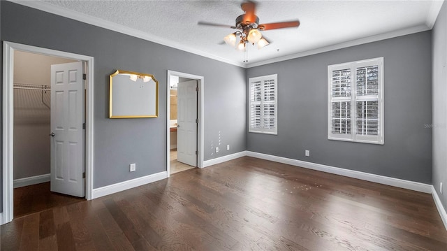 unfurnished bedroom featuring ensuite bathroom, a walk in closet, a textured ceiling, ornamental molding, and dark hardwood / wood-style floors