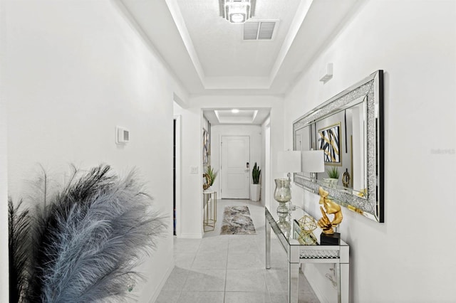 hallway with a raised ceiling and light tile patterned floors