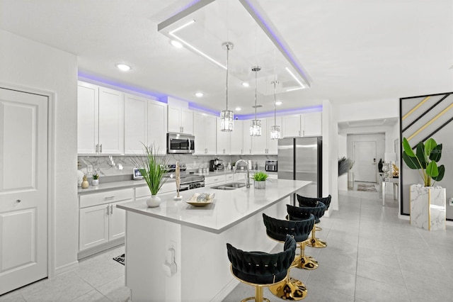 kitchen with sink, a breakfast bar area, stainless steel appliances, an island with sink, and white cabinets