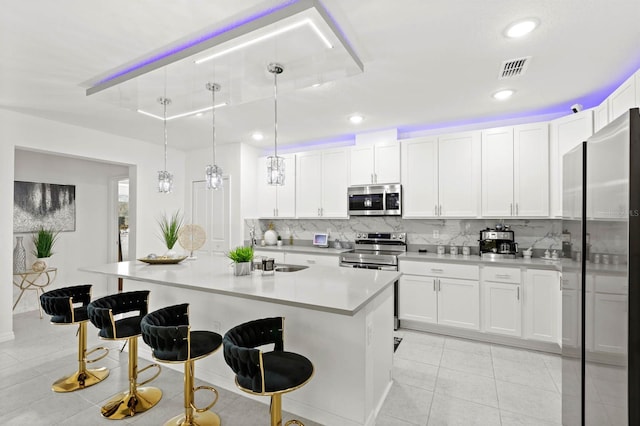 kitchen featuring white cabinetry, hanging light fixtures, stainless steel appliances, and an island with sink