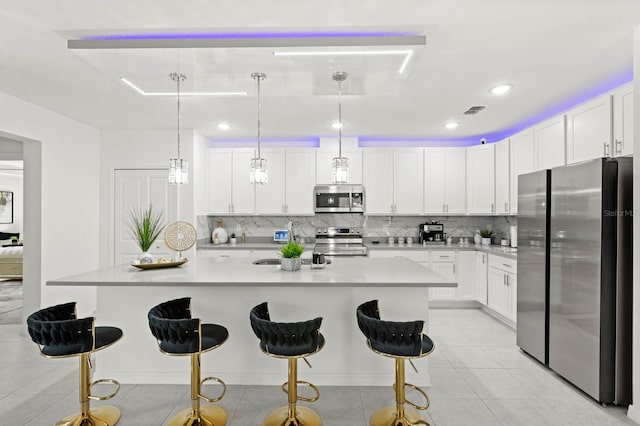 kitchen featuring pendant lighting, white cabinetry, stainless steel appliances, a kitchen breakfast bar, and an island with sink