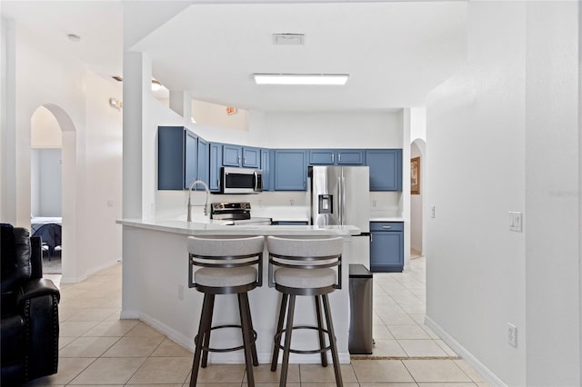 kitchen with a breakfast bar area, blue cabinetry, stainless steel appliances, light tile patterned flooring, and kitchen peninsula