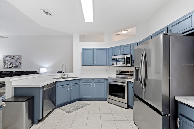 kitchen with sink, appliances with stainless steel finishes, blue cabinets, light tile patterned flooring, and kitchen peninsula