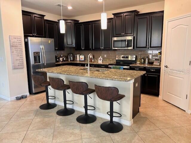 kitchen featuring appliances with stainless steel finishes, decorative light fixtures, sink, light tile patterned floors, and a center island with sink