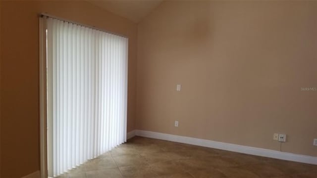 tiled spare room featuring lofted ceiling and baseboards