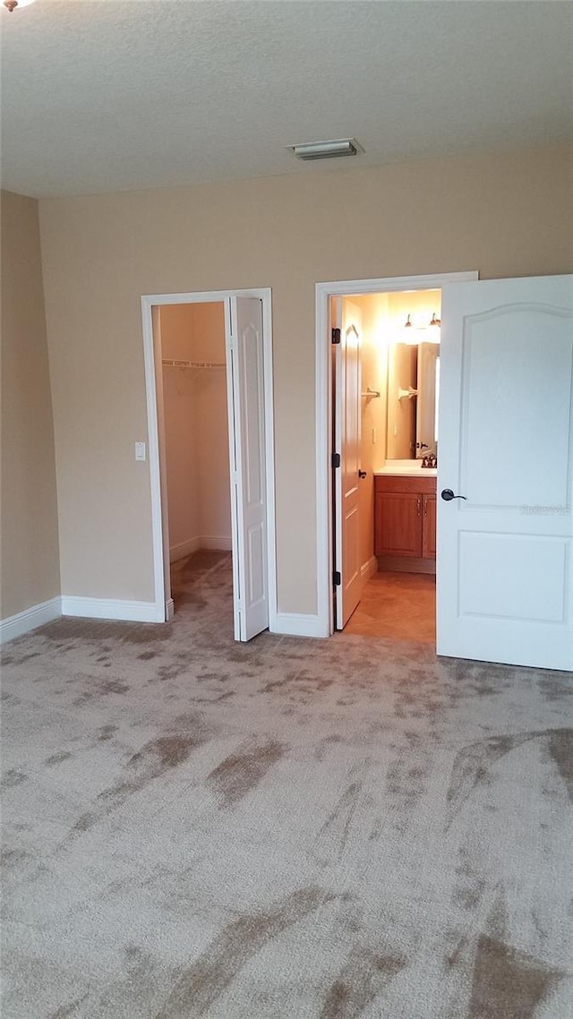 unfurnished bedroom featuring carpet, a walk in closet, visible vents, and baseboards