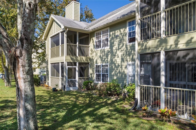 back of property with a sunroom, a yard, a chimney, and a balcony