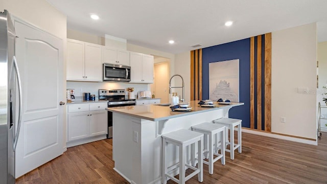 kitchen with a breakfast bar, an island with sink, white cabinetry, stainless steel appliances, and light hardwood / wood-style flooring