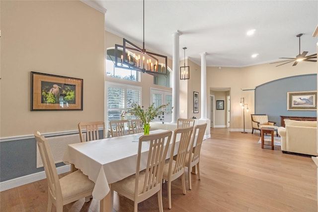 dining area featuring a towering ceiling, ceiling fan with notable chandelier, ornamental molding, and light wood-type flooring