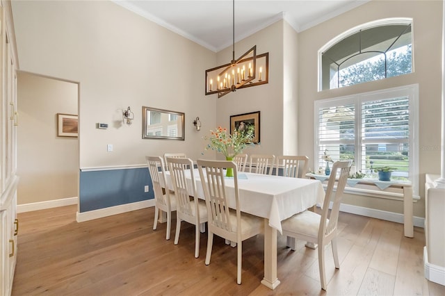 dining space with a notable chandelier, ornamental molding, light hardwood / wood-style floors, and a high ceiling