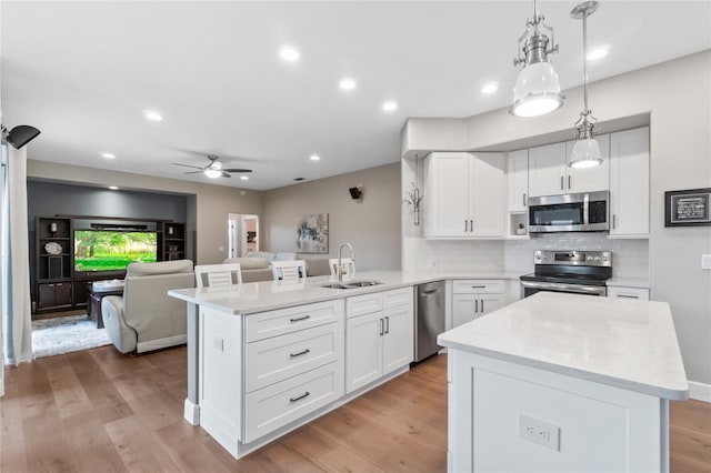 kitchen with sink, hanging light fixtures, kitchen peninsula, stainless steel appliances, and white cabinets