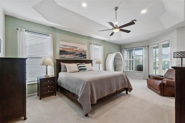 bedroom featuring ceiling fan, a tray ceiling, and light carpet