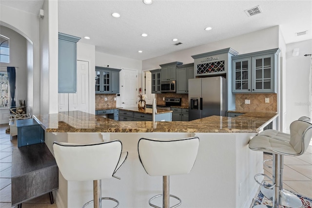 kitchen with appliances with stainless steel finishes, dark stone counters, a kitchen bar, and kitchen peninsula