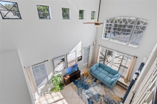 living room featuring light tile patterned flooring, ceiling fan, a towering ceiling, and a wealth of natural light