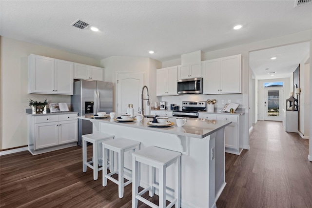 kitchen with stainless steel appliances, an island with sink, a breakfast bar, and white cabinetry